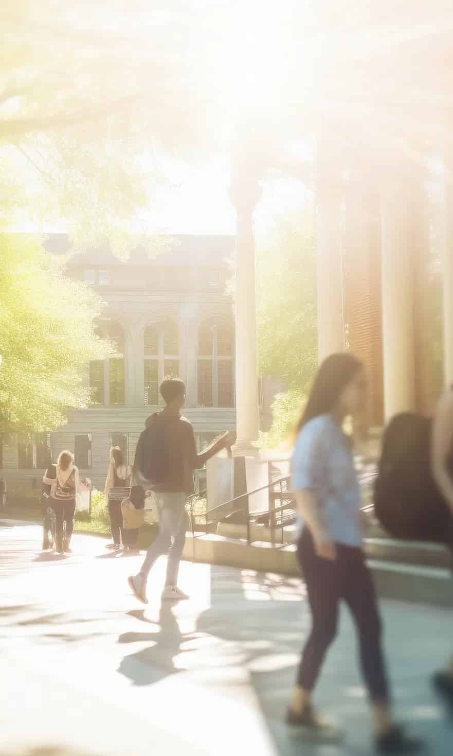 Studenten gehen auf einem sonnigen Campusgelände vor einem historischen Gebäude entlang, umgeben von grünen Bäumen.
